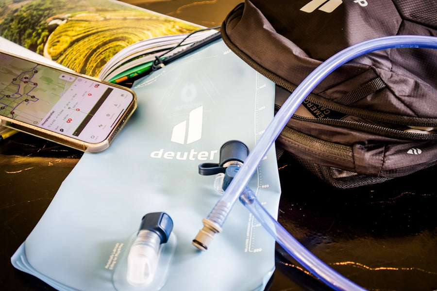 Hydration backpack water bladder reservoir with drinking hose beside a hiking pack and trail map