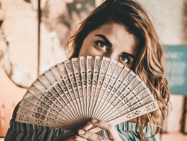 Woman holding an open carved bamboo and paper folding hand fan in front of her face