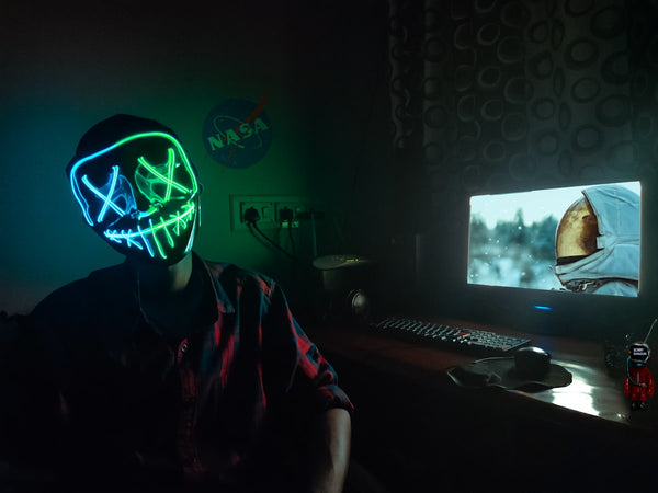 Person wearing a blue and green LED neon light-up face mask in a dark room