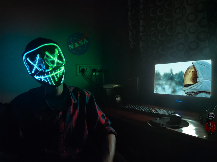 Person wearing a blue and green LED neon light-up face mask in a dark room