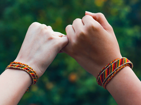 Two wrists stacked with colorful woven beaded kandi-style rave bracelets