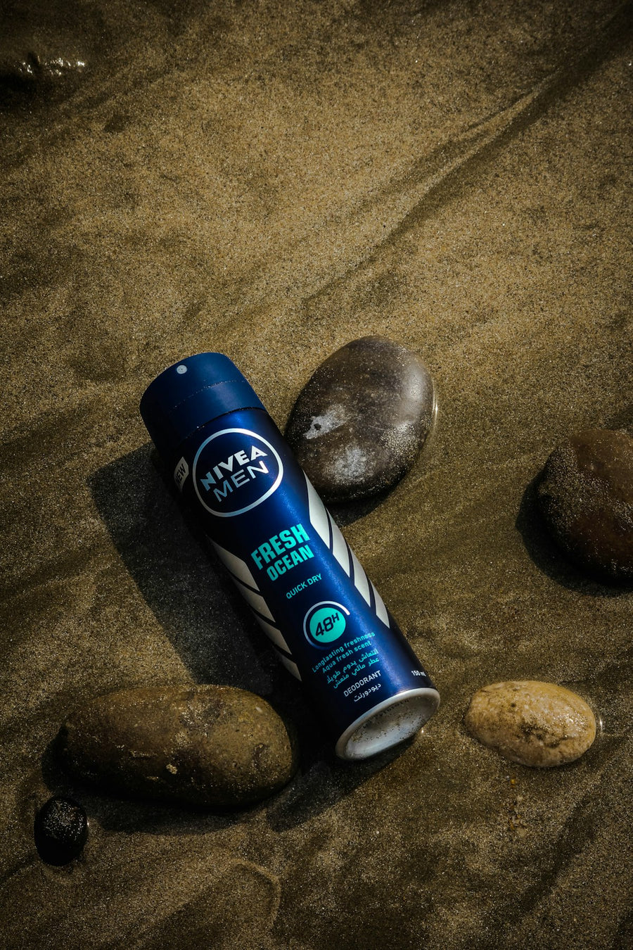 Travel-size deodorant body spray can resting on sand among stones