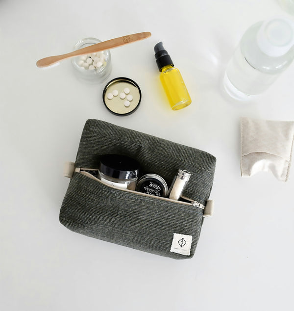 Travel toiletry bag with travel-size bottles, dropper, and tins laid out flat